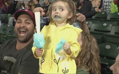 A little girl enjoying cotton candy at a baseball game.